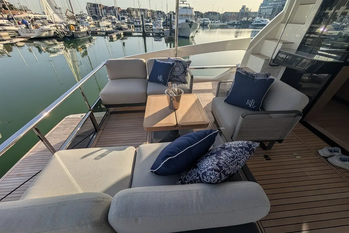 Stylish yacht deck featuring plush seating, a wooden table, and a champagne bucket with a marina backdrop.